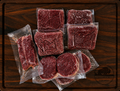 The Ranch Starter Box from Pierce Land & Bison showing four vacuum-sealed 1 lb packages of grass-fed ground bison, two packages of bison burger patties, and one package of New York strip steak arranged on a dark walnut cutting board