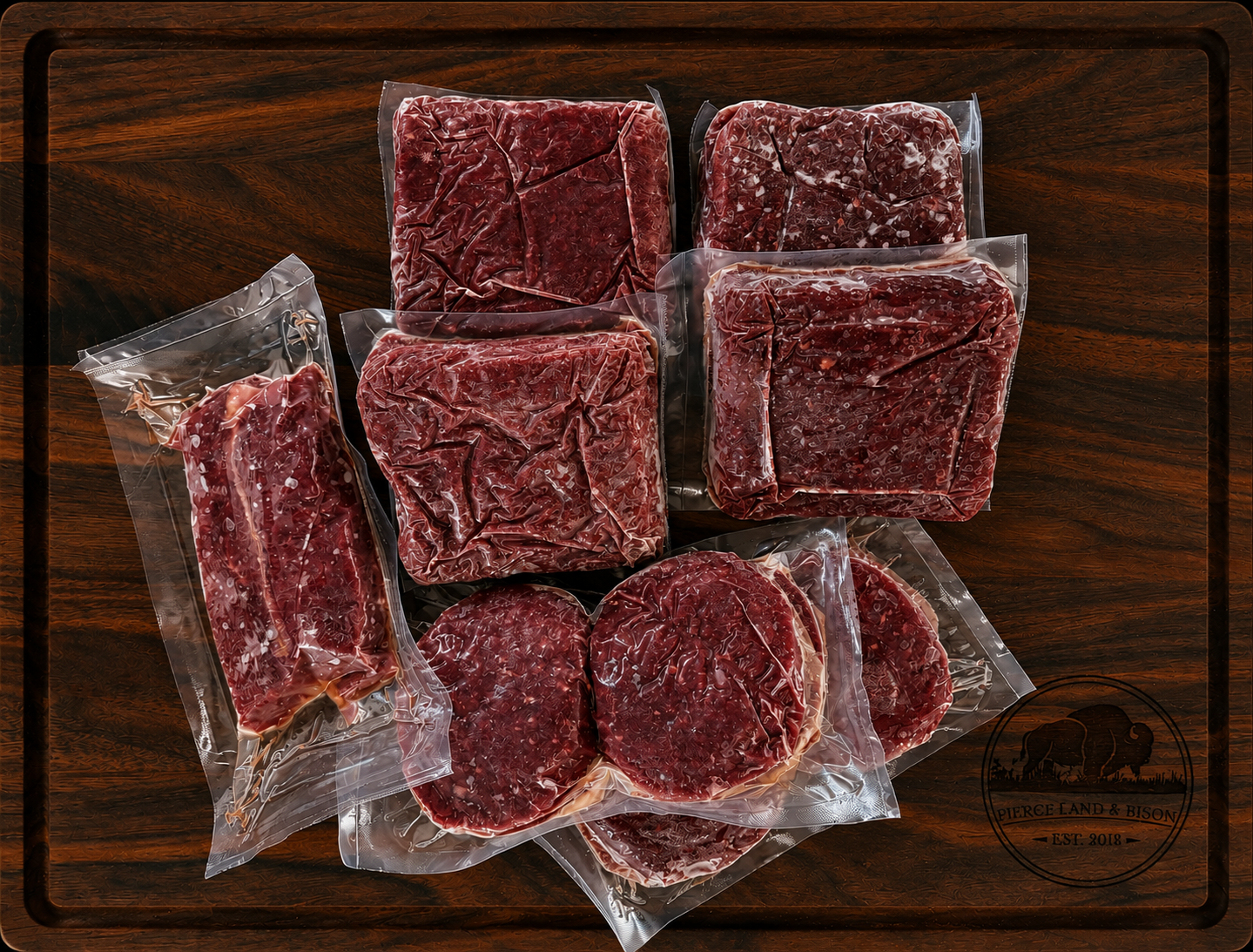 The Ranch Starter Box from Pierce Land & Bison showing four vacuum-sealed 1 lb packages of grass-fed ground bison, two packages of bison burger patties, and one package of New York strip steak arranged on a dark walnut cutting board